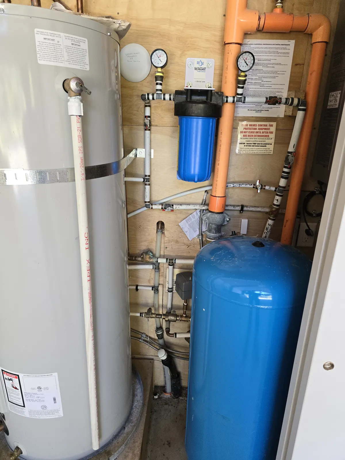 Before: old closet with a water heater, filter, blue pressure tank and orange fire sprinkler pipe
