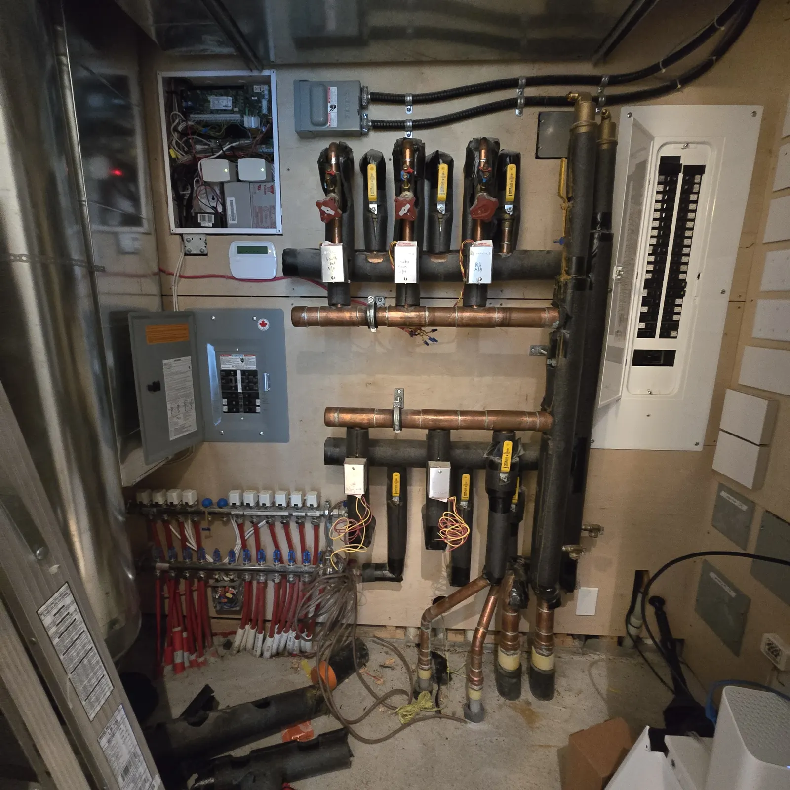 Before: old copper headers with zone valves beside the electrical panel