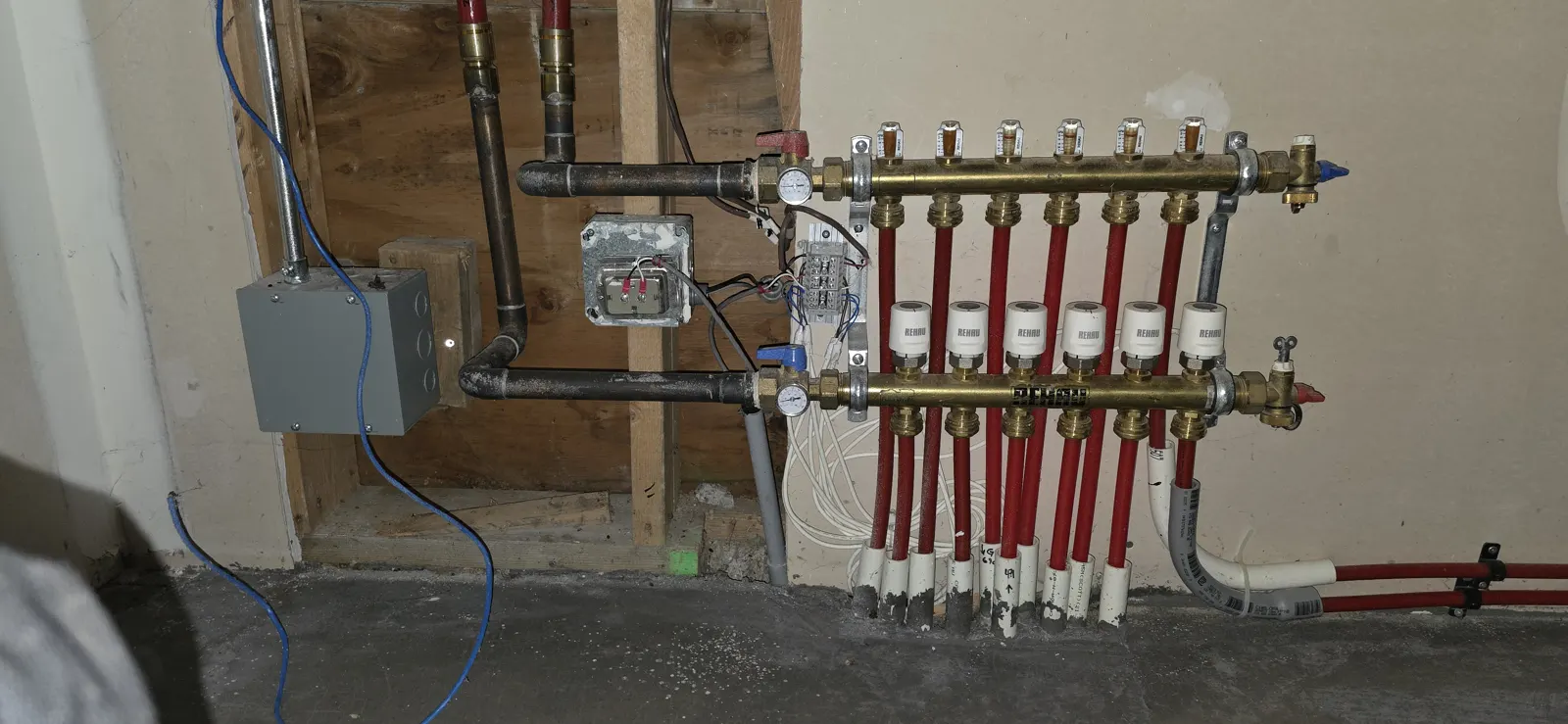 Before: old red PEX radiant manifold in a wood-framed wall