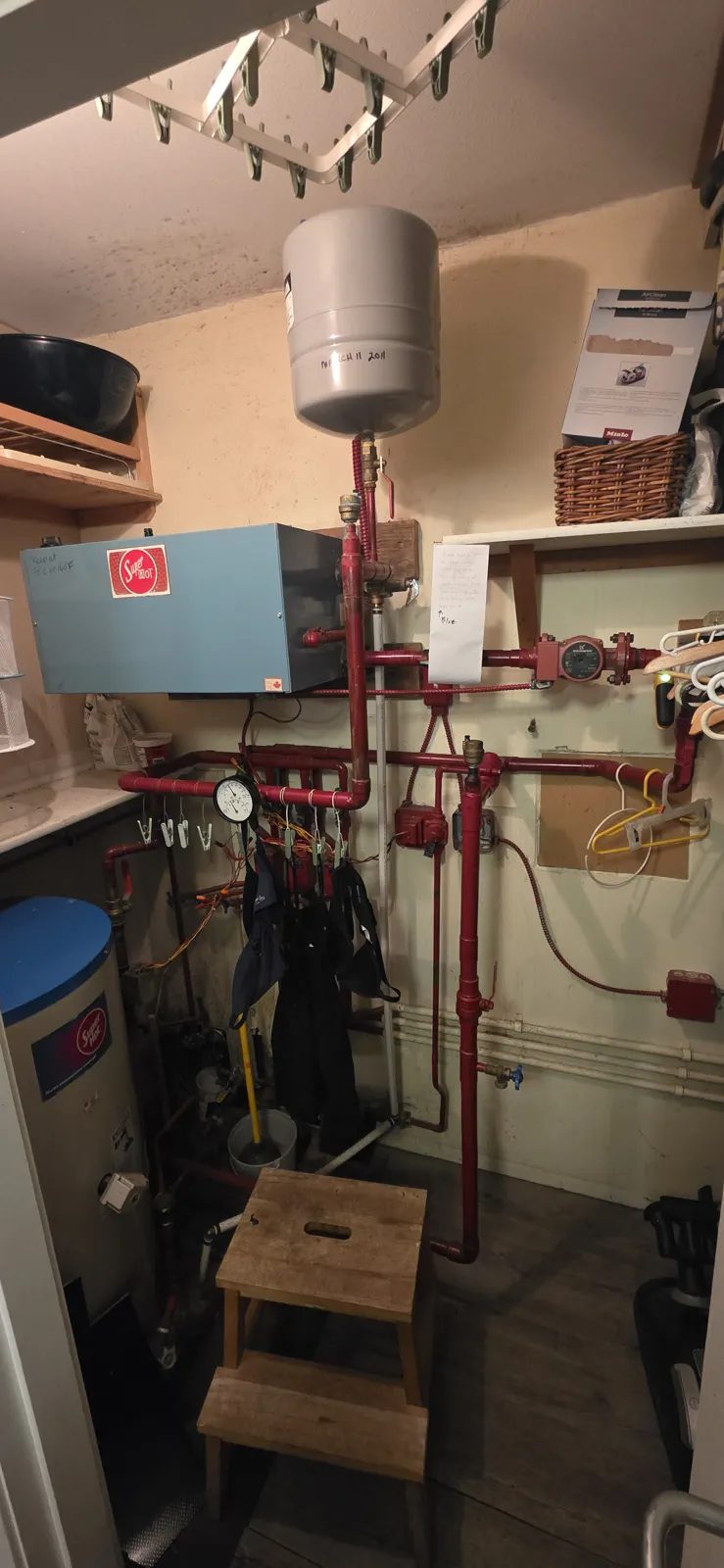 Before: old electric boiler, red-painted piping and expansion tank in a cramped closet