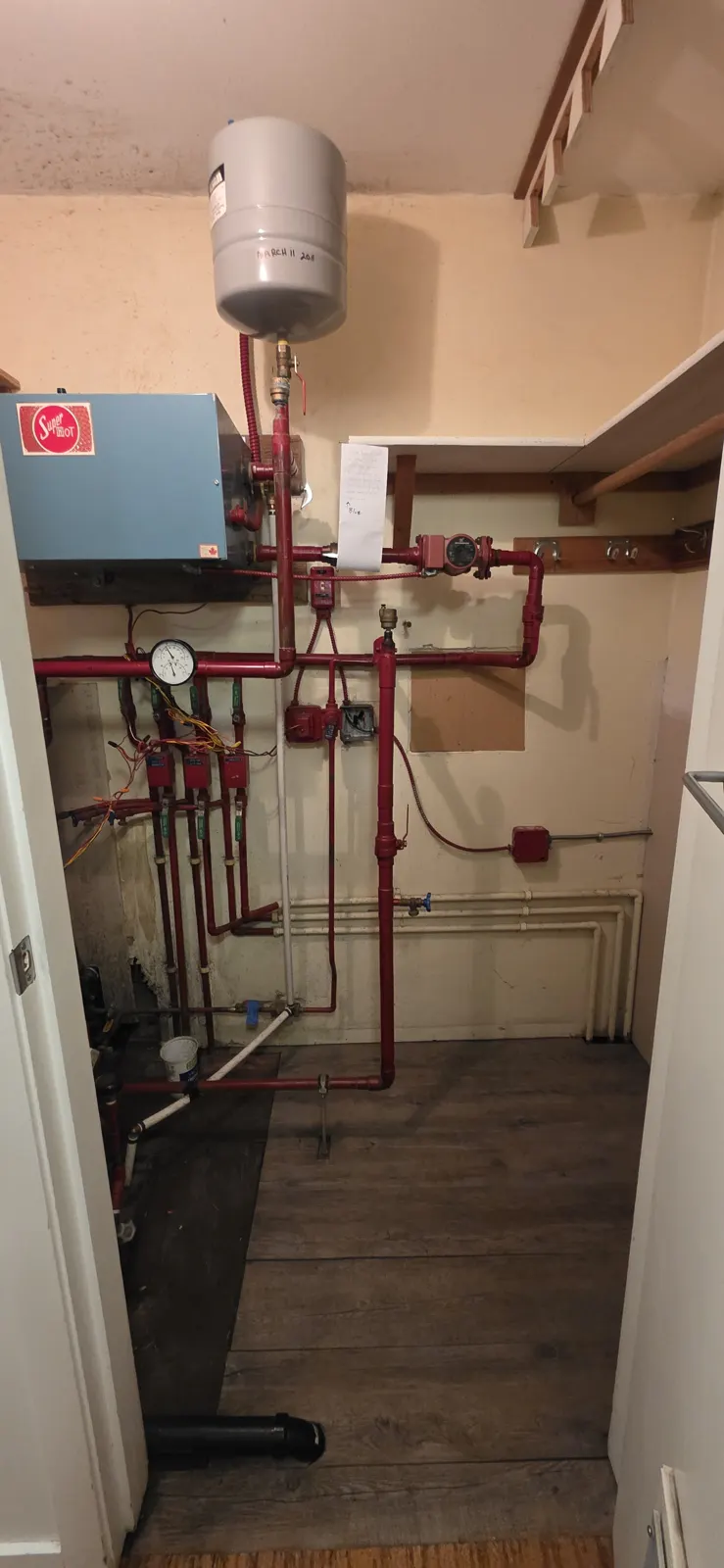Before: old electric boiler and red-painted piping on the closet wall
